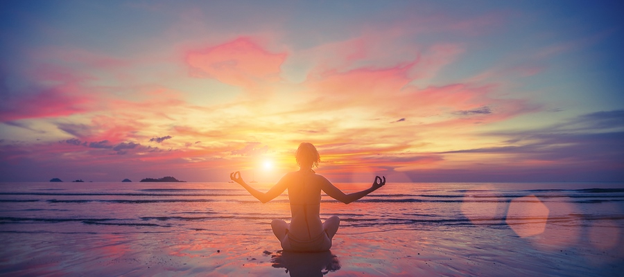 Woman doing meditation near the ocean beach. Yoga silhouette.